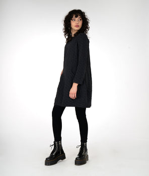 model is wearing a black dress with black leggings and boots