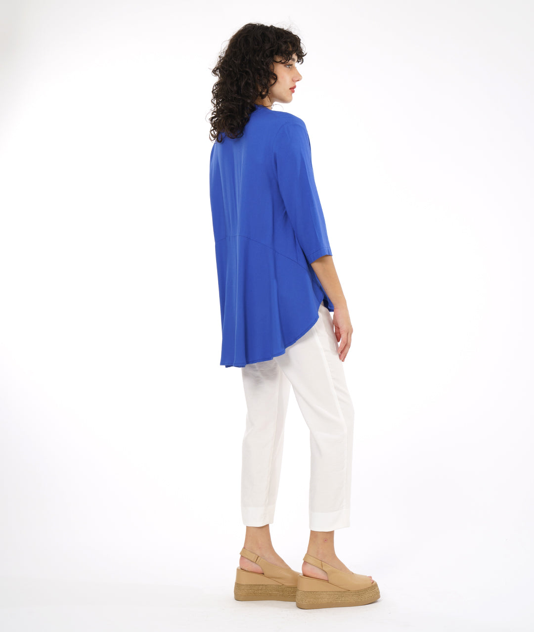 model in a white slim cut pant with a periwinkle button down blouse with 3/4 sleeves and a rounded hem, lower in the back