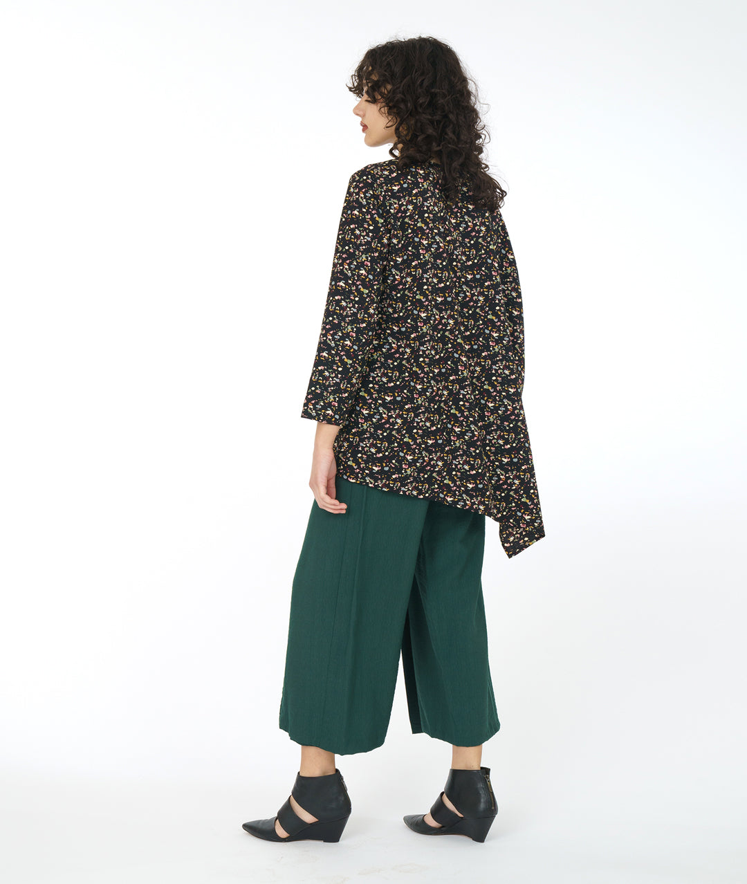 model in a wide leg forrest green pant with a black terrazzo print top. Top is asymmetrical with a drape and cocoon sleeve on one side only