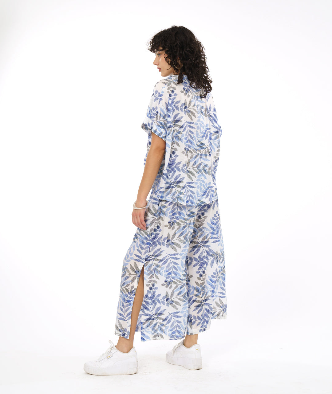 model in a white boxy pullover with a blue and black leaf print. worn with a matching wide leg pant with a slit up either side