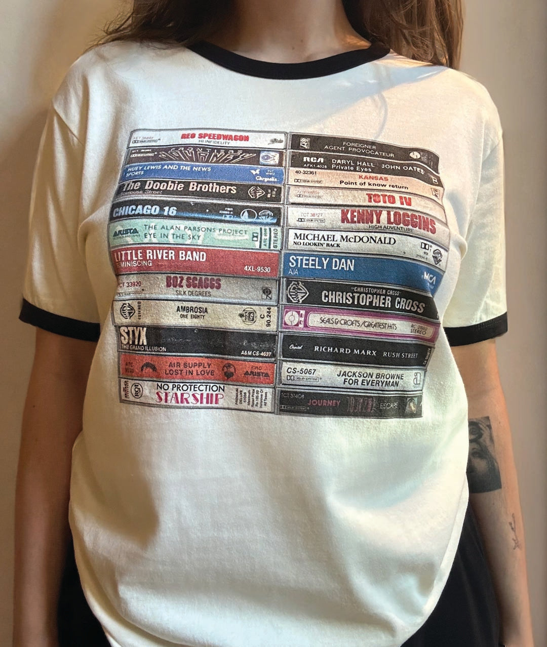 White t-shirt with black ringer sleeves and a graphic design of album covers on a plain background