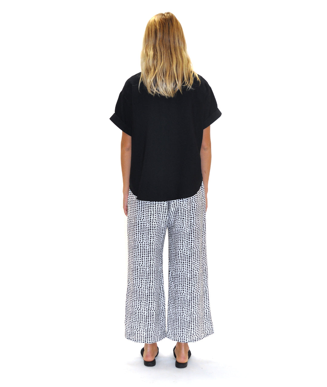 model in a black a white dot print pant with a solid black top with a vneck and pleat down the center front