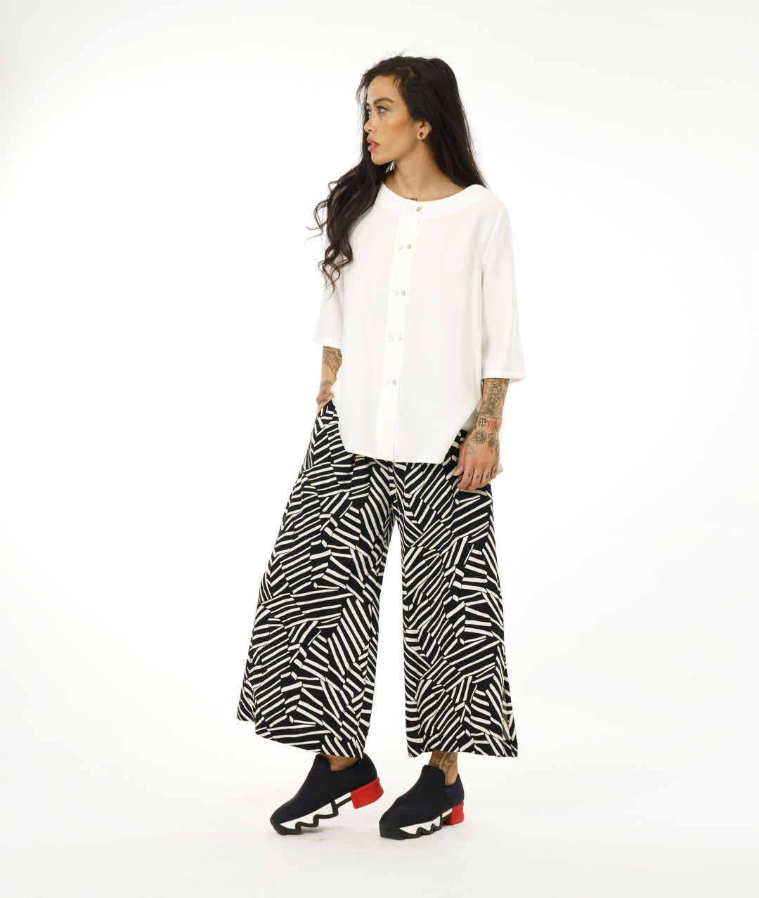 model in a black and white broken stripe print pant with a long slit at the side seams, worn with a collar less white button down blouse with 3/4 sleeves