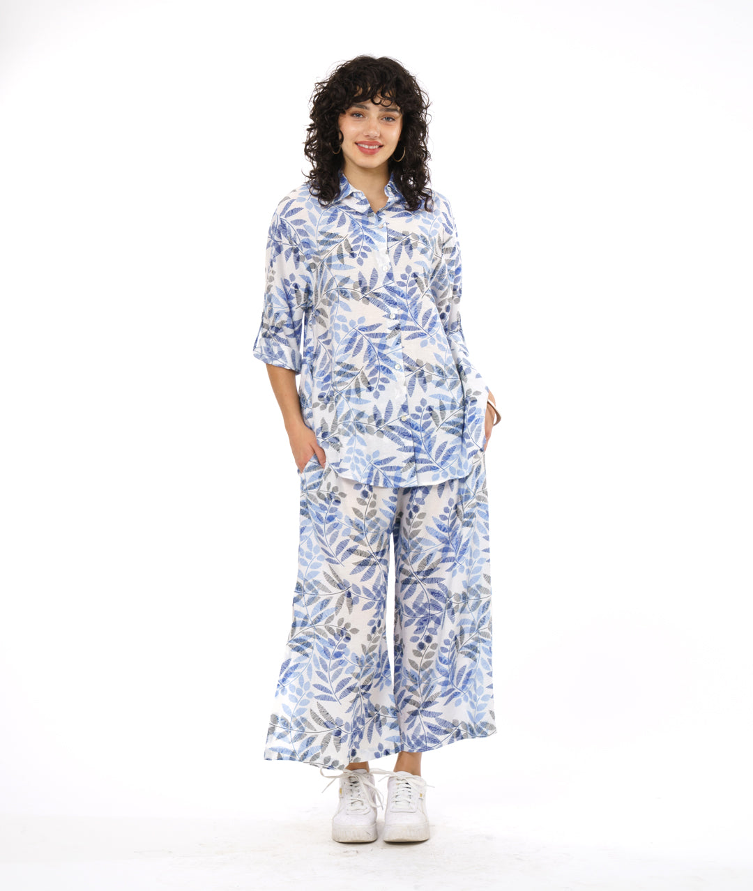model in a wide leg white pant with a blue and black leaf print. worn with a button down blouse with rolled sleeves in the same fabric