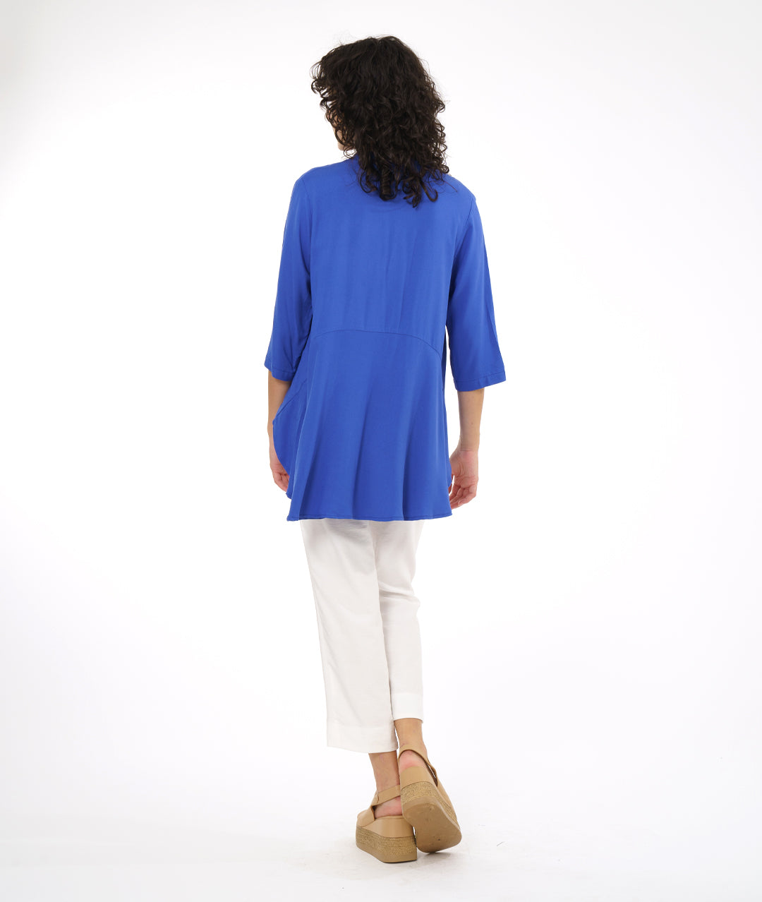 model in a white slim cut pant with a periwinkle button down blouse with 3/4 sleeves and a rounded hem, lower in the back