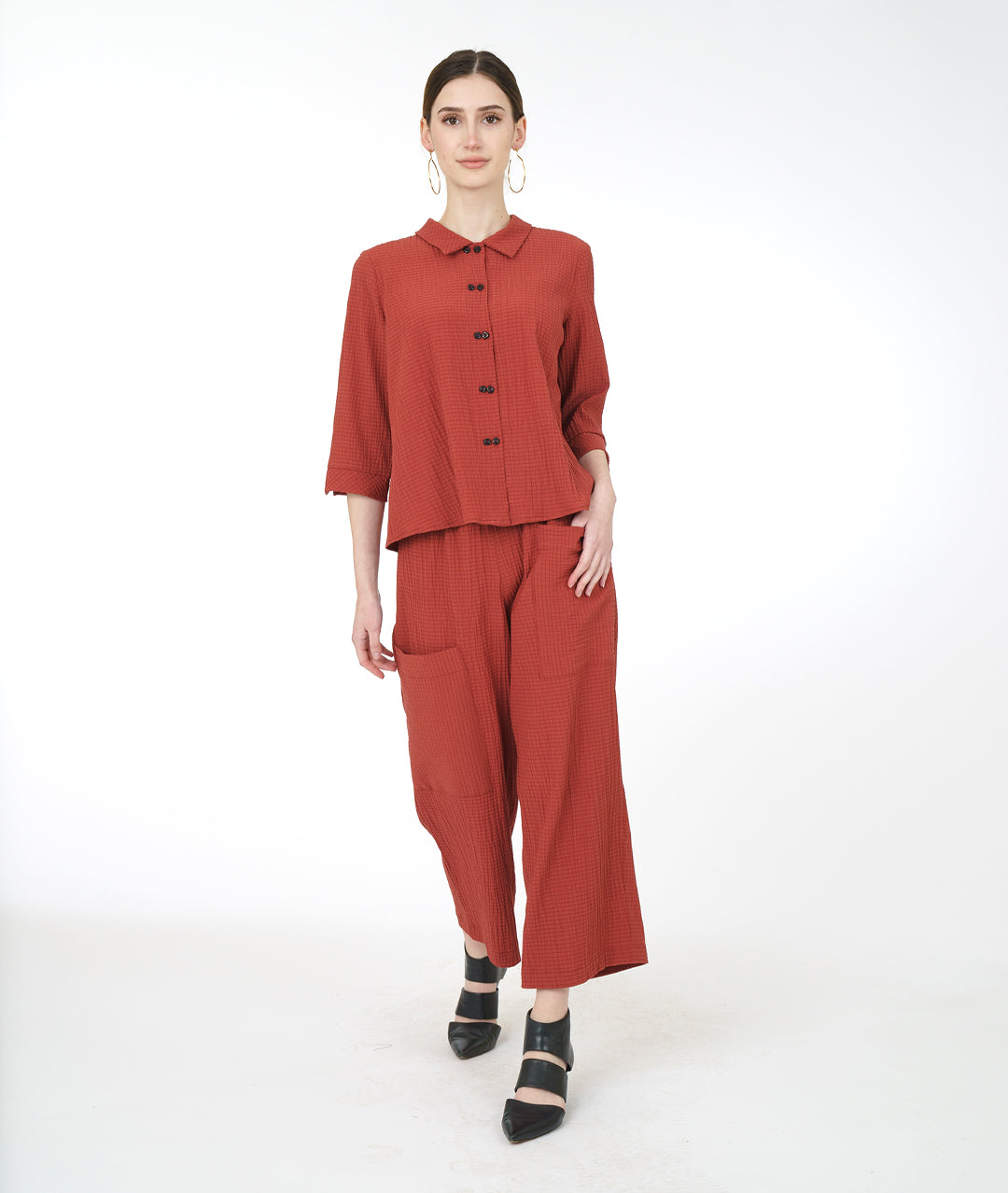 model in a sienna color pant with asymmetrical cargo pockets, worn with a matching button down top with 3/4 sleeves and a twin button detail up the front