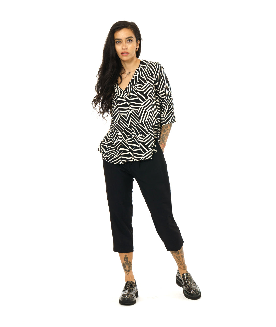 model in a black and white broken stripe print pullover top with 3/4 sleeves and a v-neck. worn with a simple black crop pant