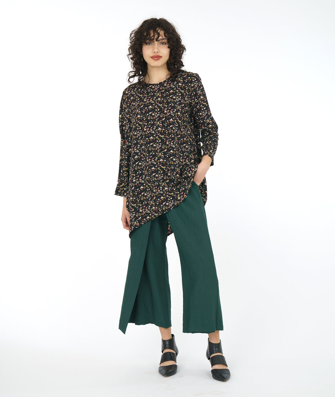 model in a wide leg forrest green pant with a black terrazzo print top. Top is asymmetrical with a drape and cocoon sleeve on one side only
