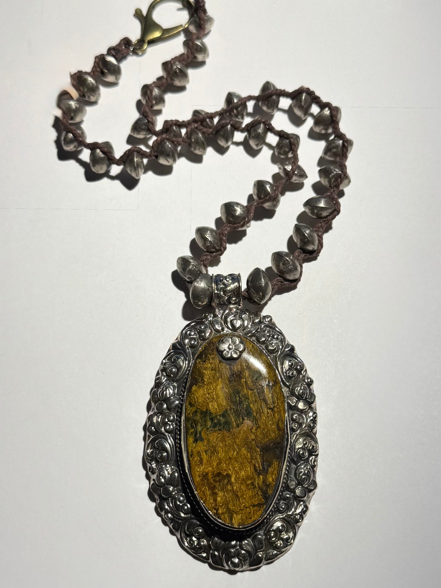 A necklace with a large brown jasper pendant set in a silver frame, surrounded by small silver beads on a chain.