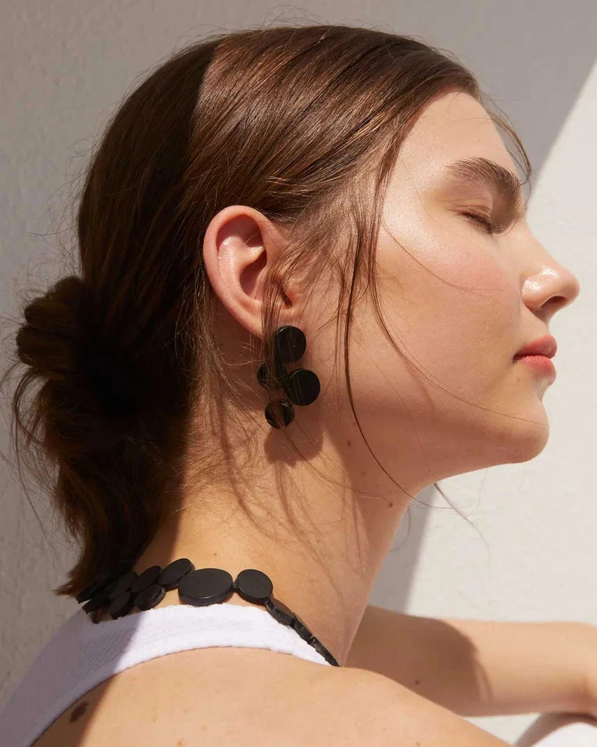 model wearing black circle cluster earrings in the sun against white background