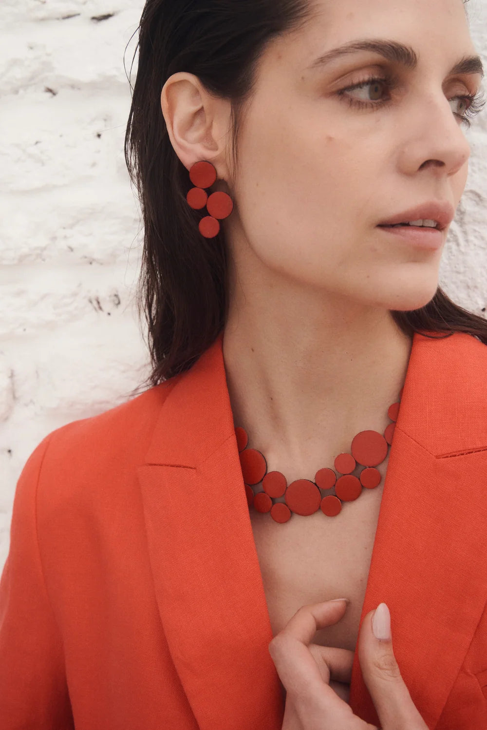 model wearing red circle cluster necklace and earring with red blazer against white rocky background