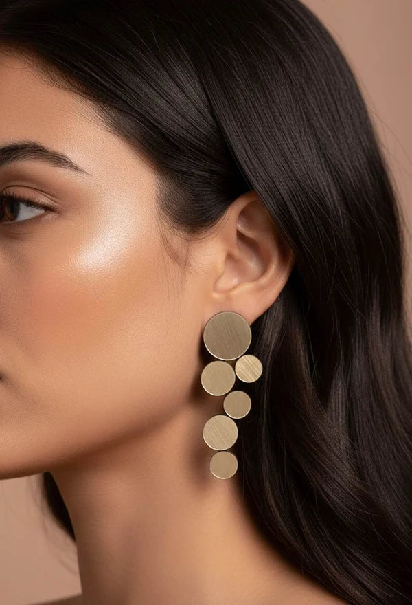 model wearing gold circle cluster earrings against light brown background
