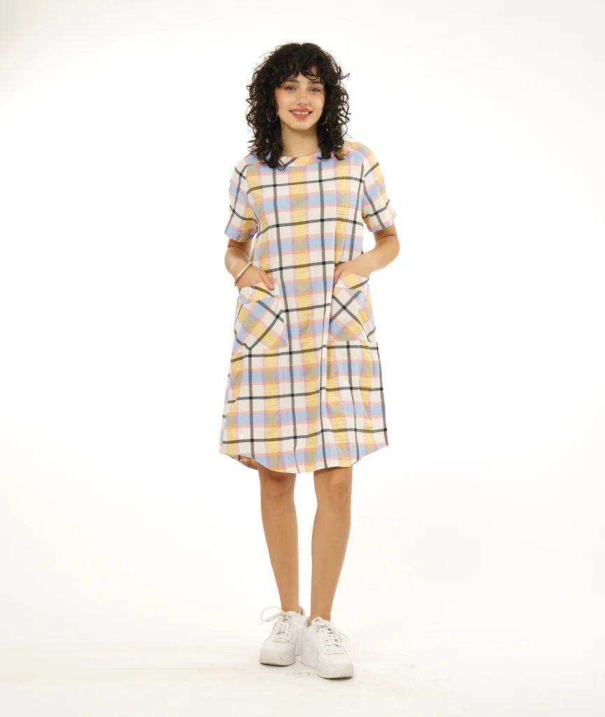 model wearing round hem dress that hits below the knee with patch pockets, short sleeves and boat neck collar in a plaid pastel pattern paired with white sneakers