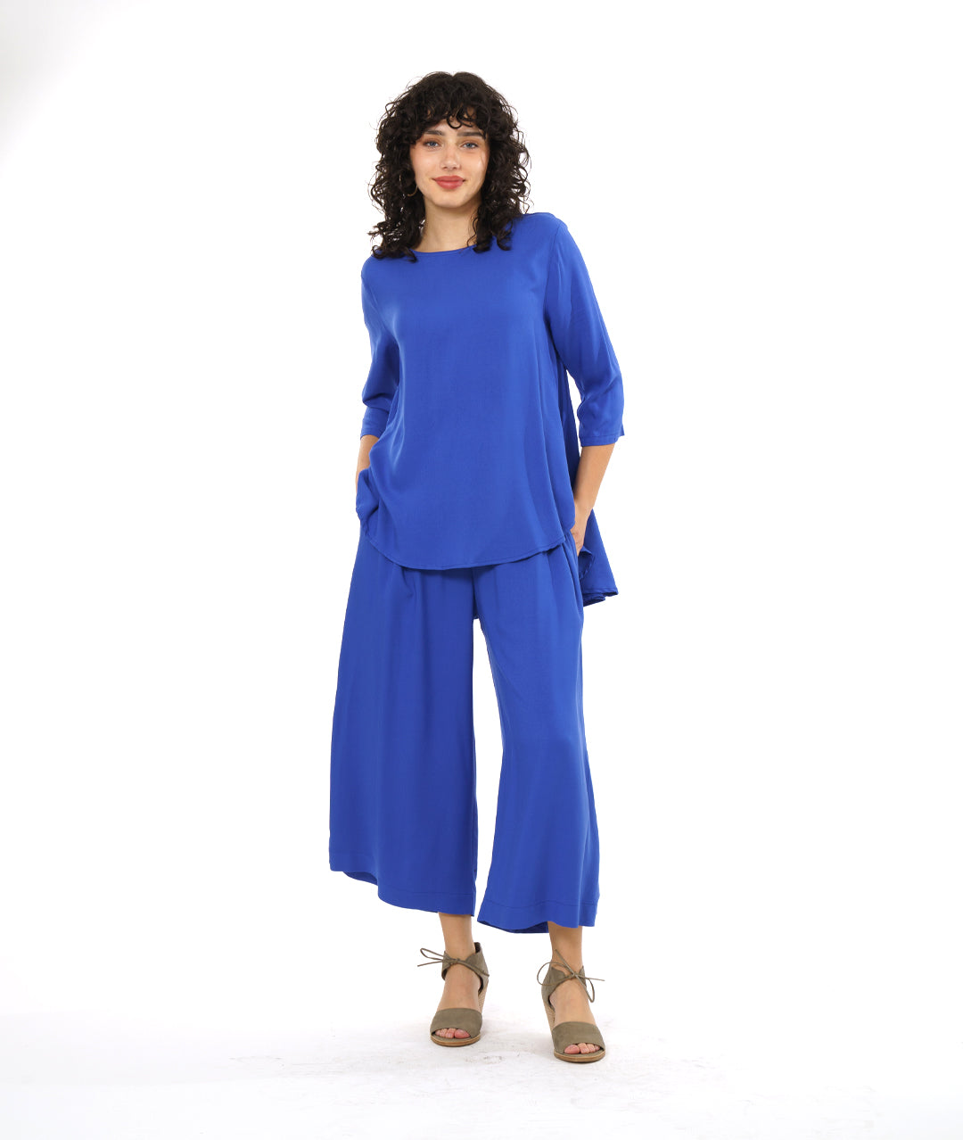 model in a wide leg periwinkle pant with a side slit on either side, worn with a matching pullover top with 3/4 sleeves and a rounded hem, dipping lower in the back