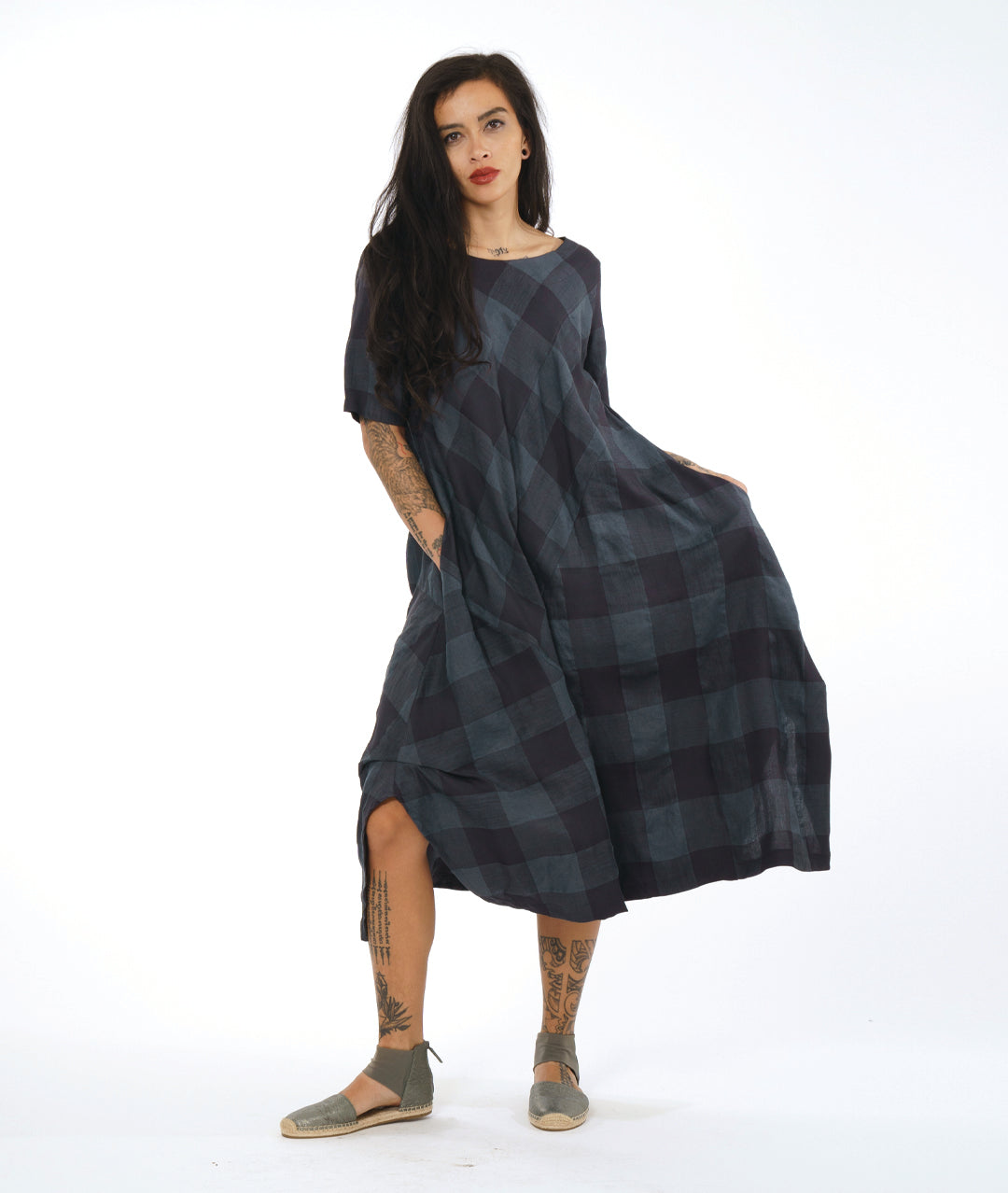 model in a midi length dress with short sleeves, a round neckline and tucks at the sides. dress has a large grid print on shades of deep gray with multi directional panels