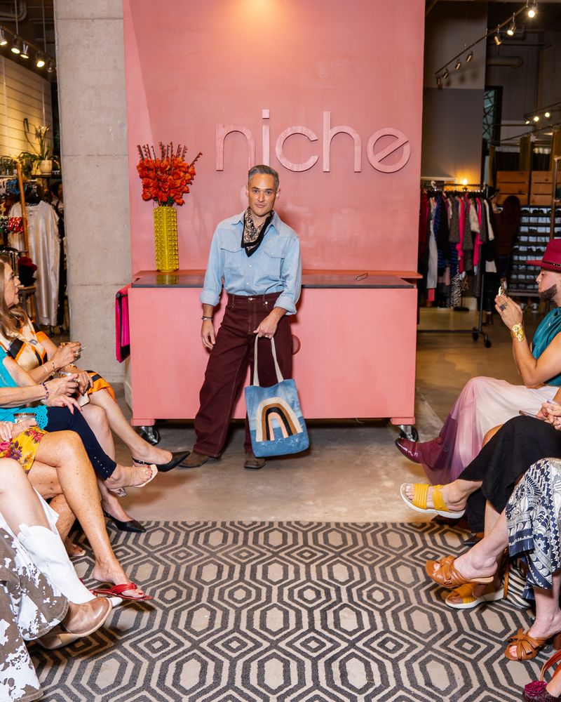 model wearing light blue pearl snap shirt with bandana, burgundy pants and jean tote with rainbow design on a runway
