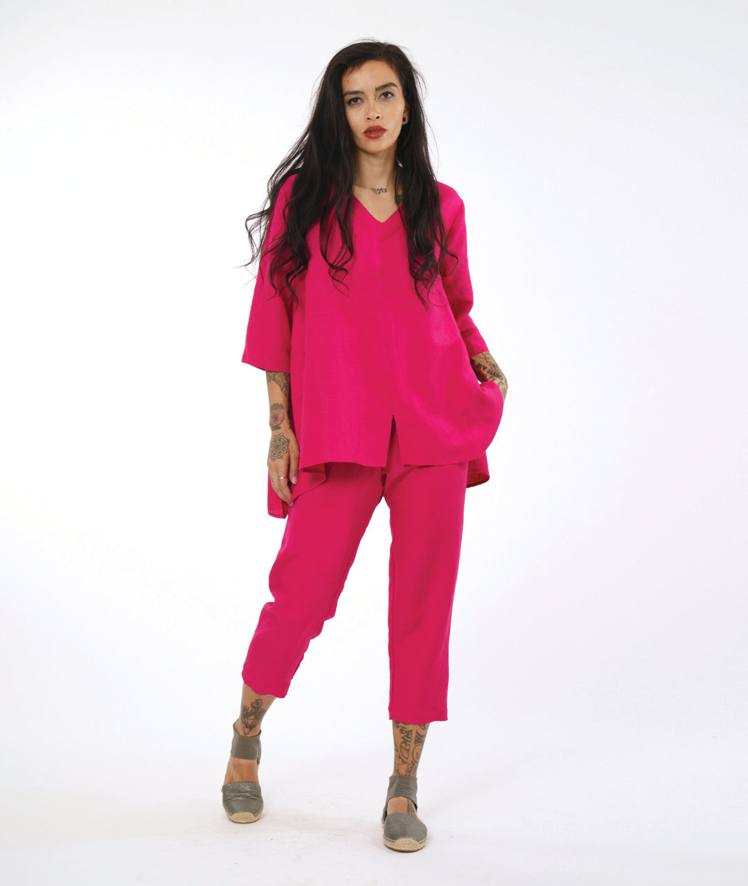 model in a hot pink pullover top with a dipped side hem, side seam pockets, 3/4 sleeves and a vneck. worn with a matching slim crop pant