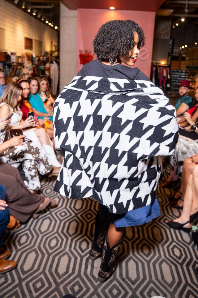 model wearing black and white houndstooth cardigan, black top, jean skirt and cowboy boots on a runway