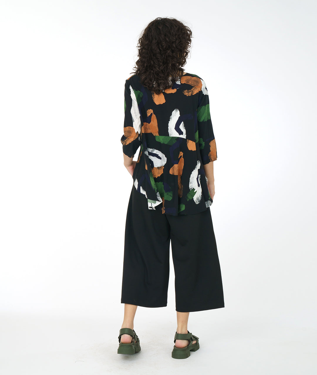 Woman wearing a patterned top and black pants on a white background