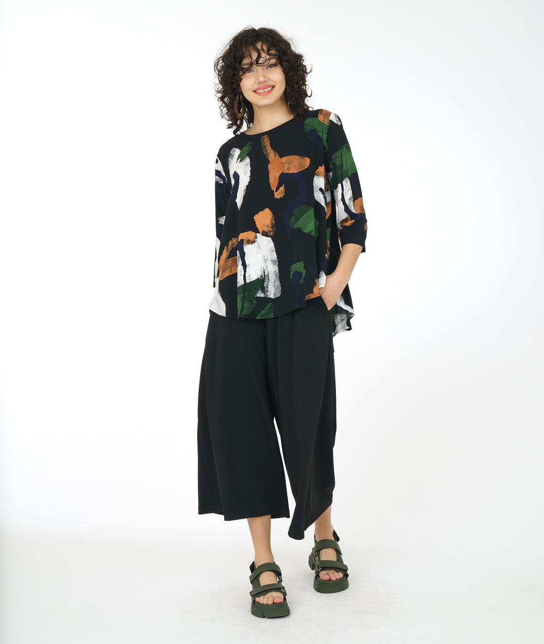 Woman wearing a patterned top and black pants on a white background