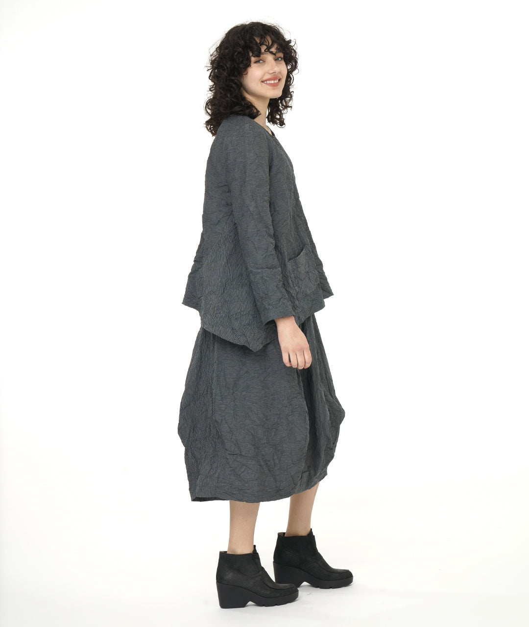 model in a black and grey pinstriped skirt with a matching pullover top with long sleeves, a single squared hip pocket, round neckline and a dip in the hem at either side