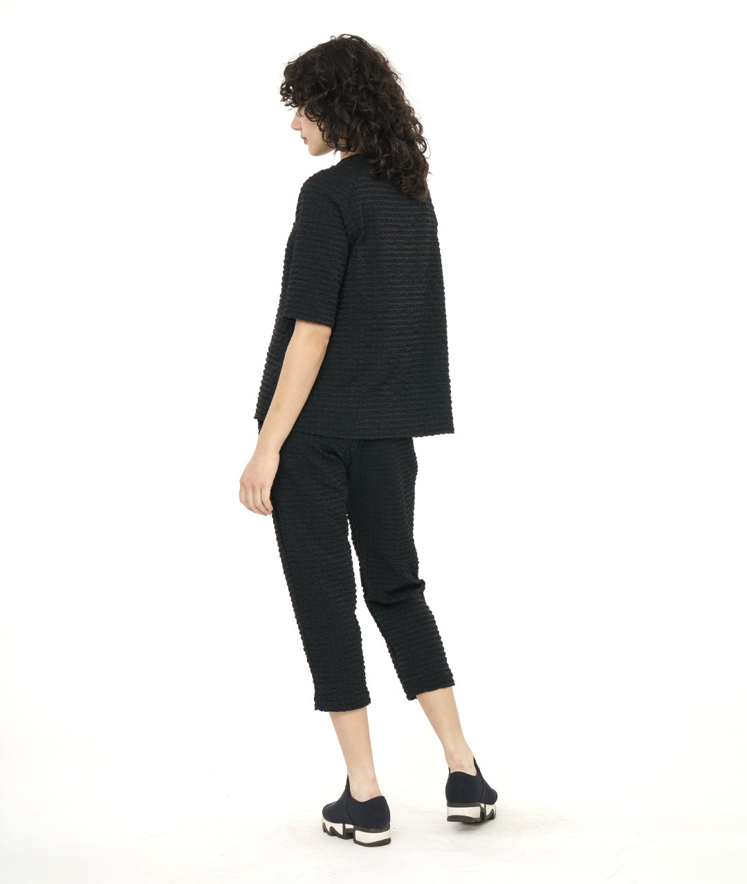 model in a black crop pant with a textured grid print. worn with a matching pullover tee with a portrait collar and a raglan sleeve
