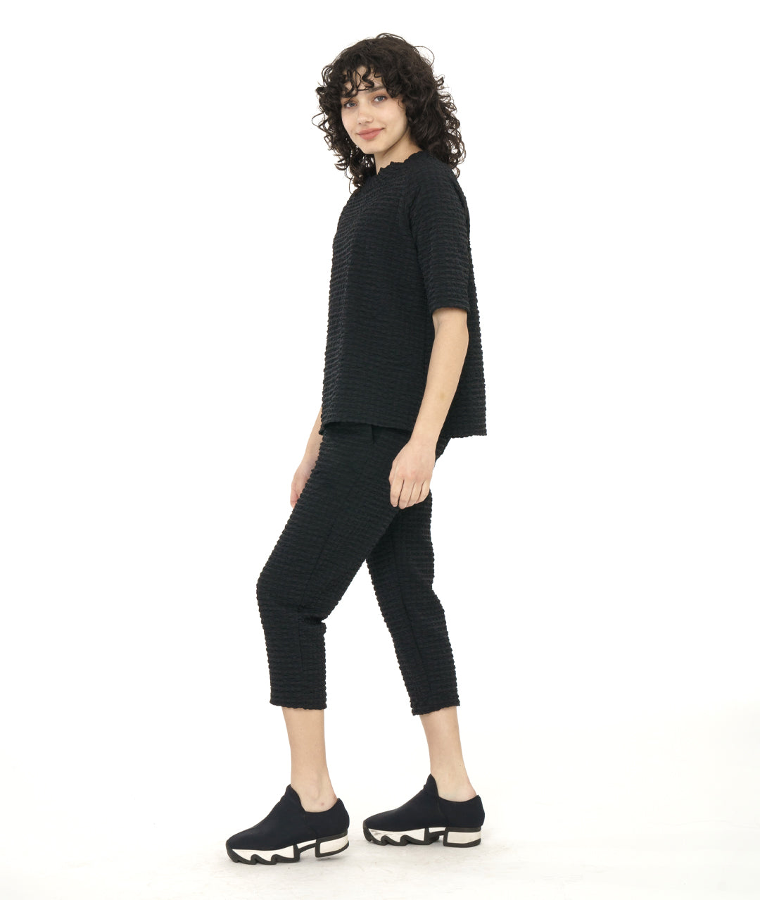 model in a black crop pant with a textured grid print. worn with a matching pullover tee with a portrait collar and a raglan sleeve