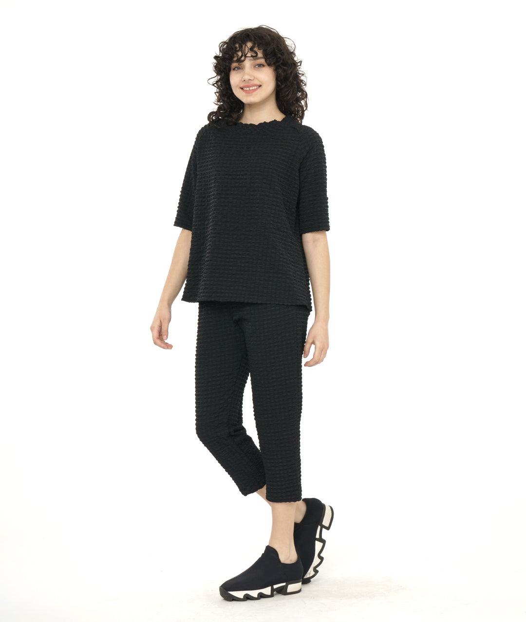 model in a black crop pant with a textured grid print. worn with a matching pullover tee with a portrait collar and a raglan sleeve