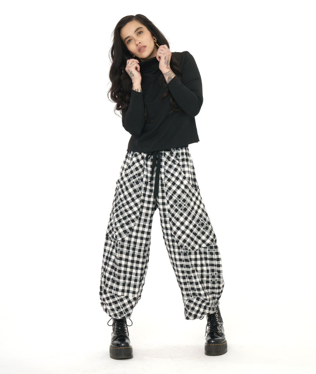 model in a black mock turtleneck top, worn with a textured black and white plaid print wide leg pant with a tapered ankle, oversized exterior pockets, and a black tie belt over the elastic waistband