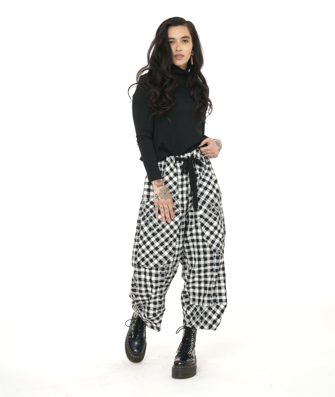 model in a black mock turtleneck top, worn with a textured black and white plaid print wide leg pant with a tapered ankle, oversized exterior pockets, and a black tie belt over the elastic waistband