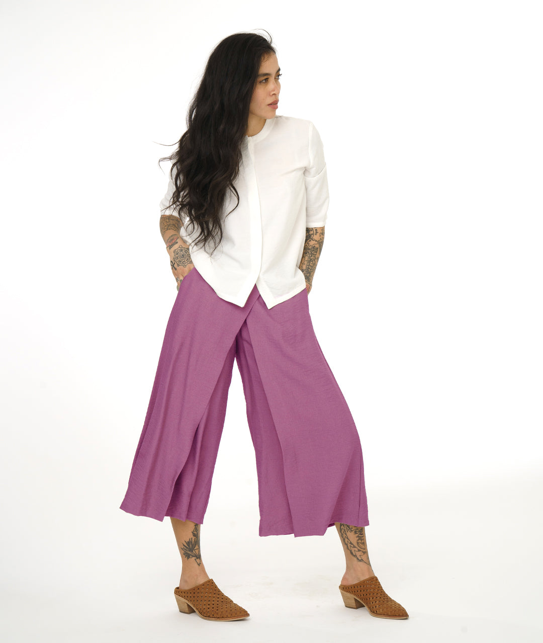 model in a white top with a hidden button placket. top has a round neckline and a 3/4 sleeve, with a small split at each hip side seam. worn with a dusty pink wide leg pant with overlapping panels