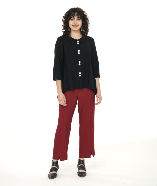 model in a black button down jacket with a 3/4 sleeve, dipped hem at the sides, and a twin button detail at the back and placket. worn with a straight leg deep red pant with a split at each ankle