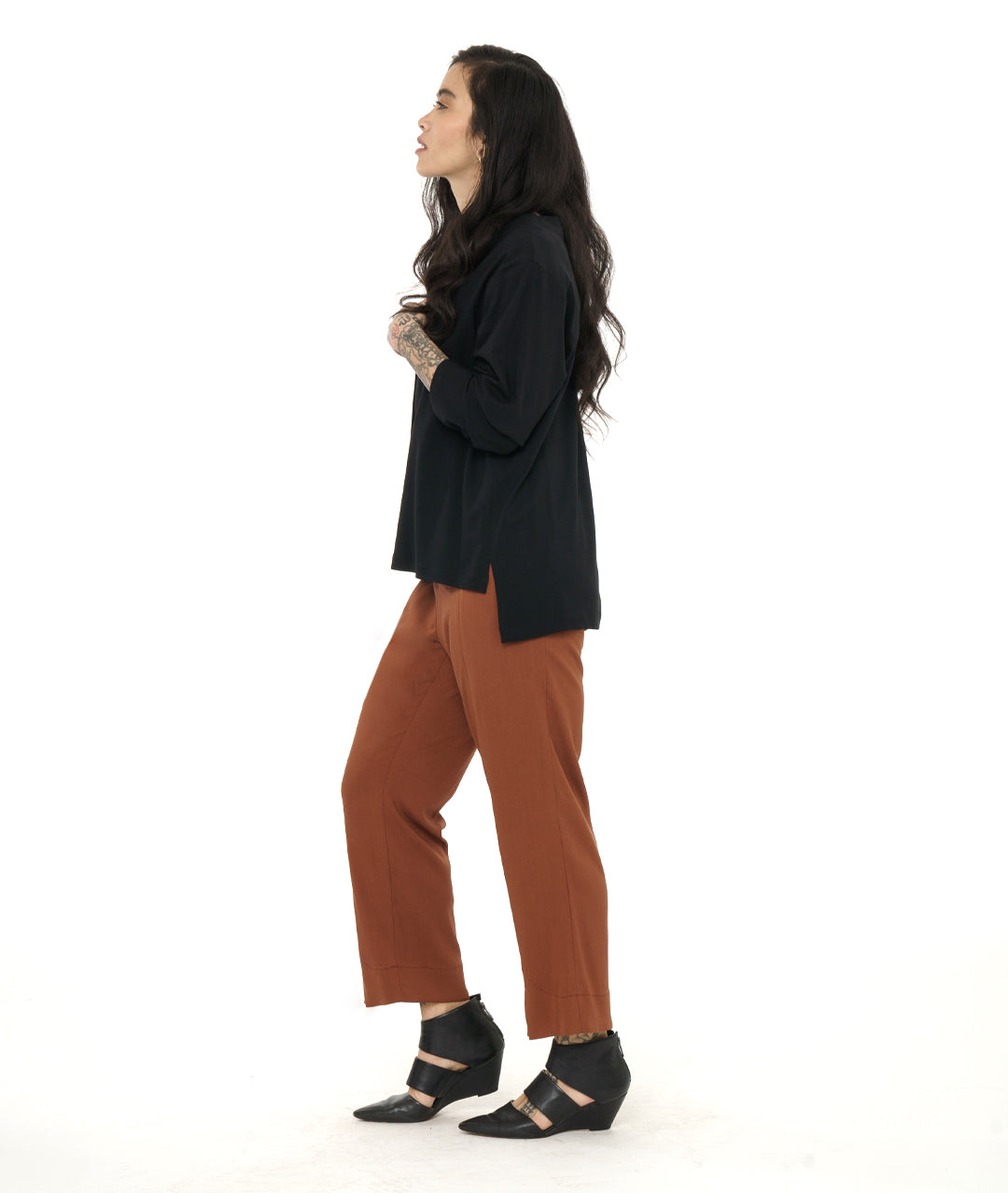 model in a rust color straight cut pant, worn with a black pullover top with long sleeves and a stair step hem