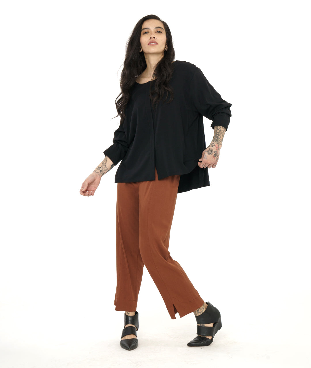 model in a rust color straight cut pant, worn with a black pullover top with long sleeves and a stair step hem