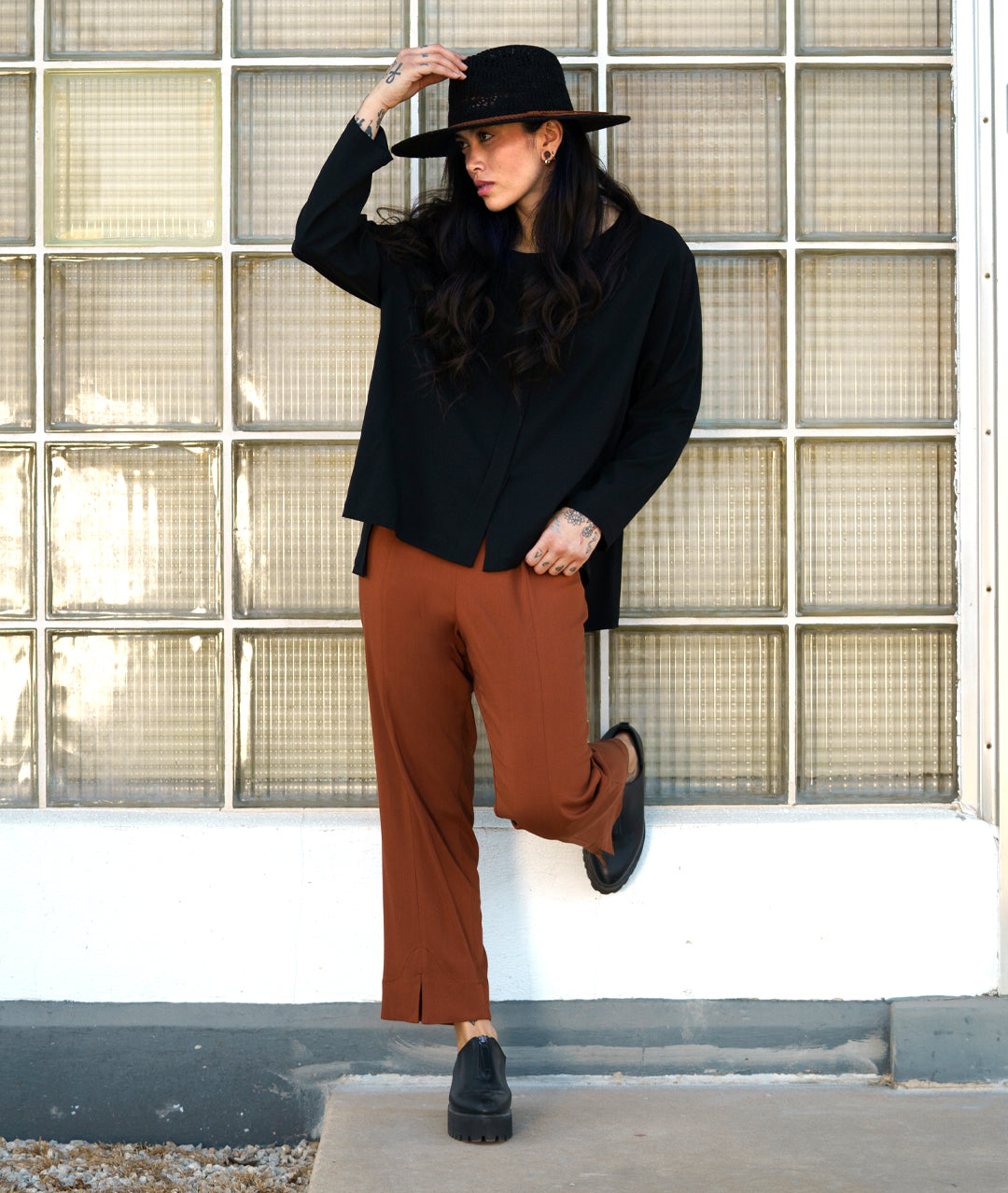 model in a rust color straight cut pant, worn with a black pullover top with long sleeves and a stair step hem
