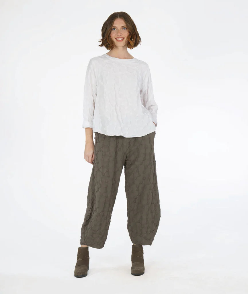 model wearing a white textured long sleeve top with green textured wide leg pants that tapers to tulip shape at ankle on a white background