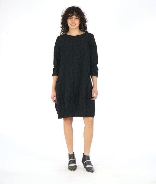 model in a black pullover, knee length dress with long sleeves and circular seams at the hips with a pocket