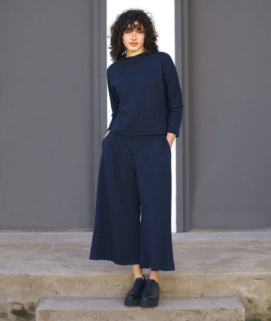 model in a black and blue zipper knit pullover top with a high neckline and dolman sleeves. worn with a matching wide leg pant