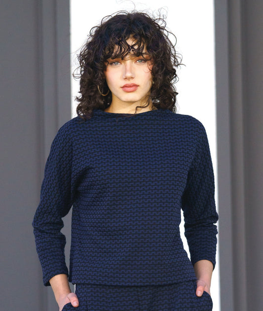 model in a black and blue zipper knit pullover top with a high neckline and dolman sleeves. worn with a matching wide leg pant