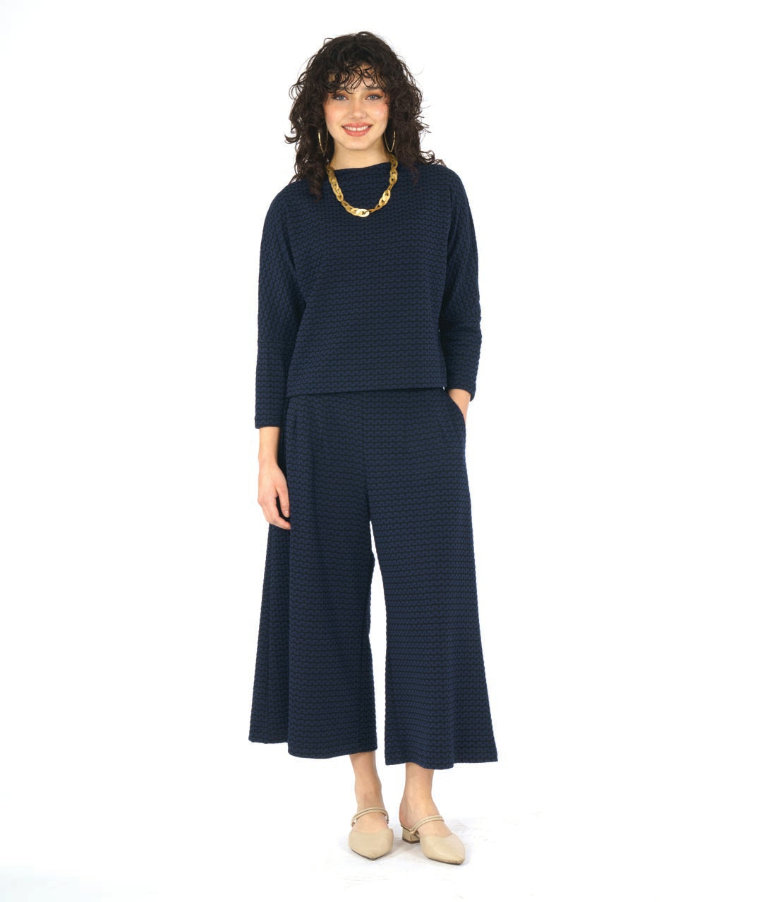 model in a black and blue zipper knit pullover top with a high neckline and dolman sleeves. worn with a matching wide leg pant