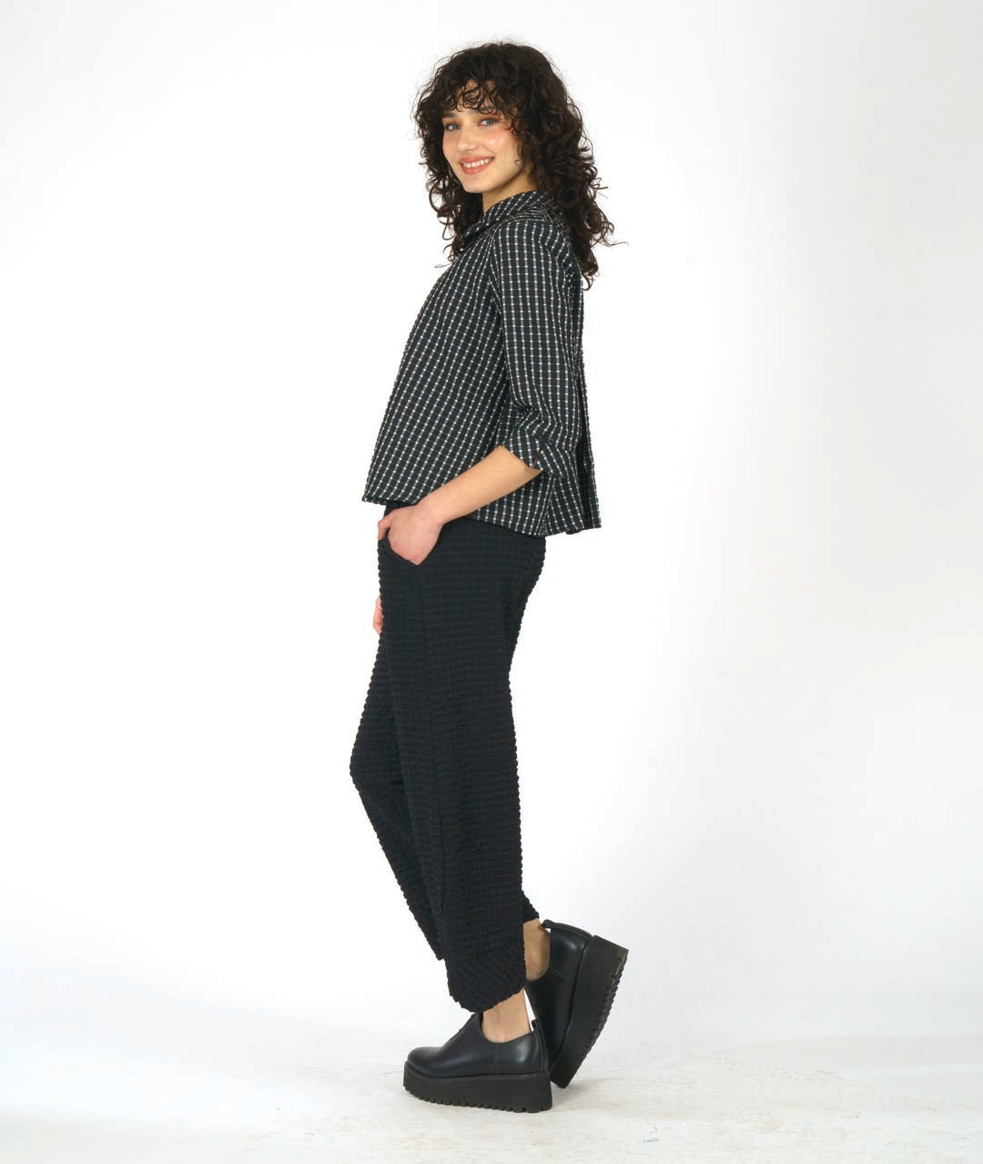 model in a black textured wide leg pant with a tapered ankle. worn with a matching black and white check print button down blouse with 3/4 sleeves and a twin button detail