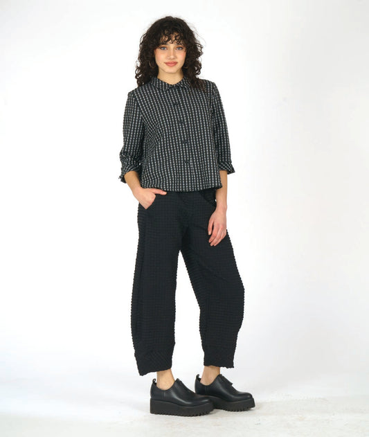 model in a black textured wide leg pant with a tapered ankle. worn with a matching black and white check print button down blouse with 3/4 sleeves and a twin button detail