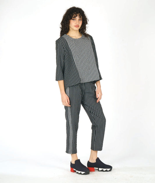 model in astraight cut black crop pants with a white grid print. tuxedo stripes on the sides in a reverse of the main body fabric. worn with a matching pullover top with 3/4 sleeves, and contrasting center panels in the front and back in the same contrast as the pant stripes