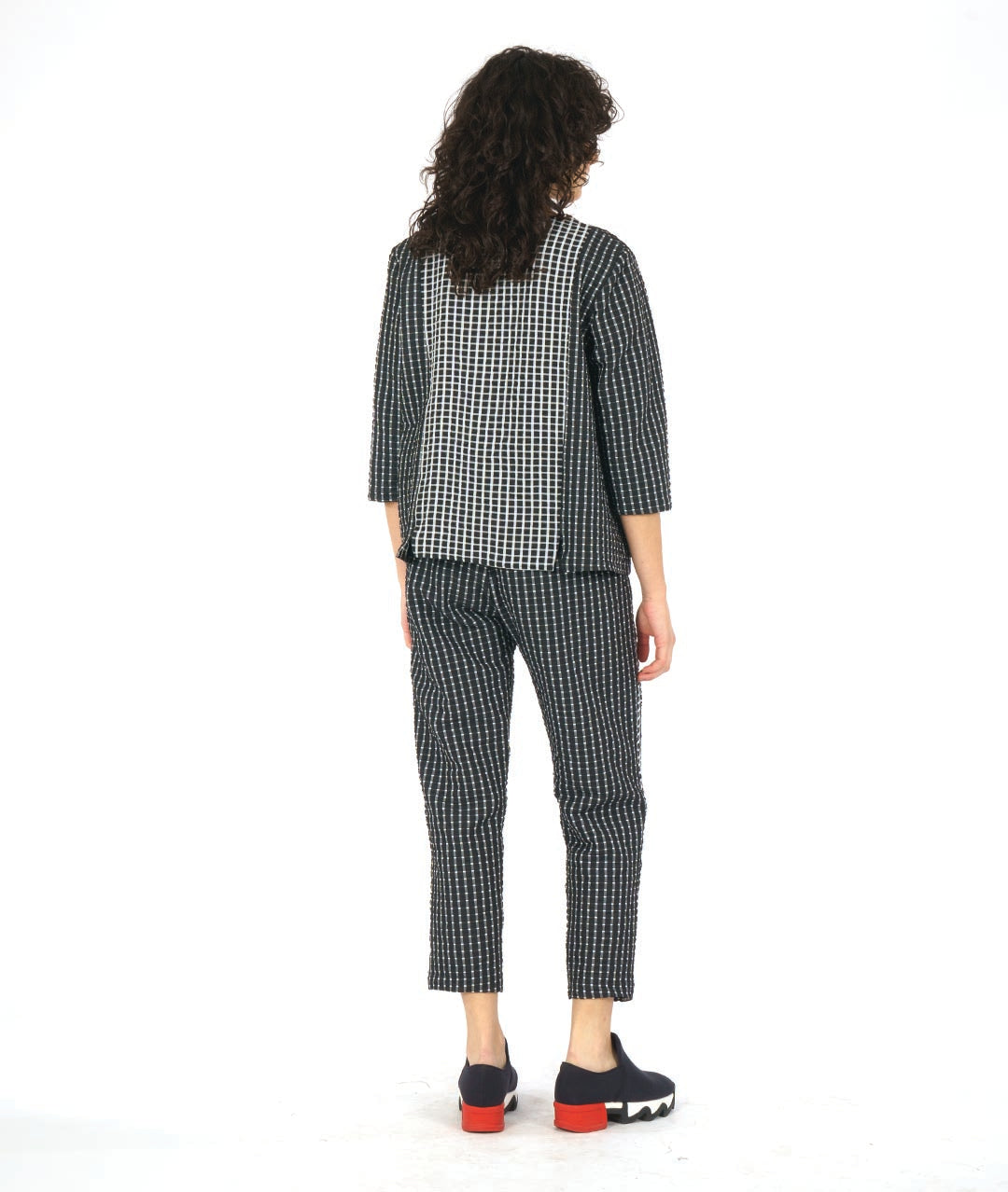 model in astraight cut black crop pants with a white grid print. tuxedo stripes on the sides in a reverse of the main body fabric. worn with a matching pullover top with 3/4 sleeves, and contrasting center panels in the front and back in the same contrast as the pant stripes