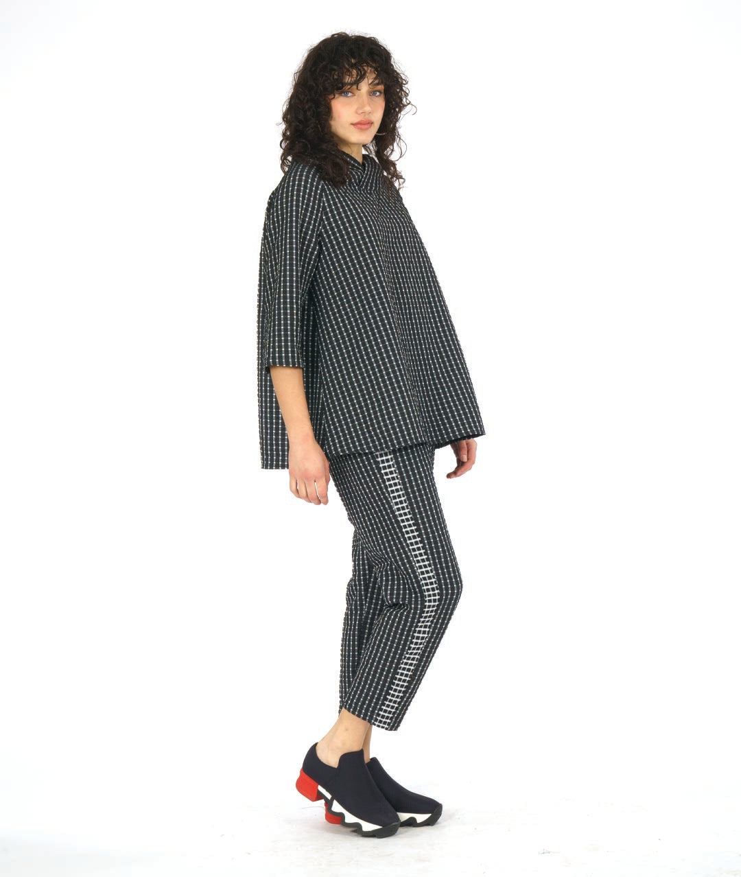 model in astraight cut black crop pants with a white grid print. tuxedo stripes on the sides in a reverse of the main body fabric. worn with a matching pullover top with an oversized, gathered collar and 3/4 sleeves