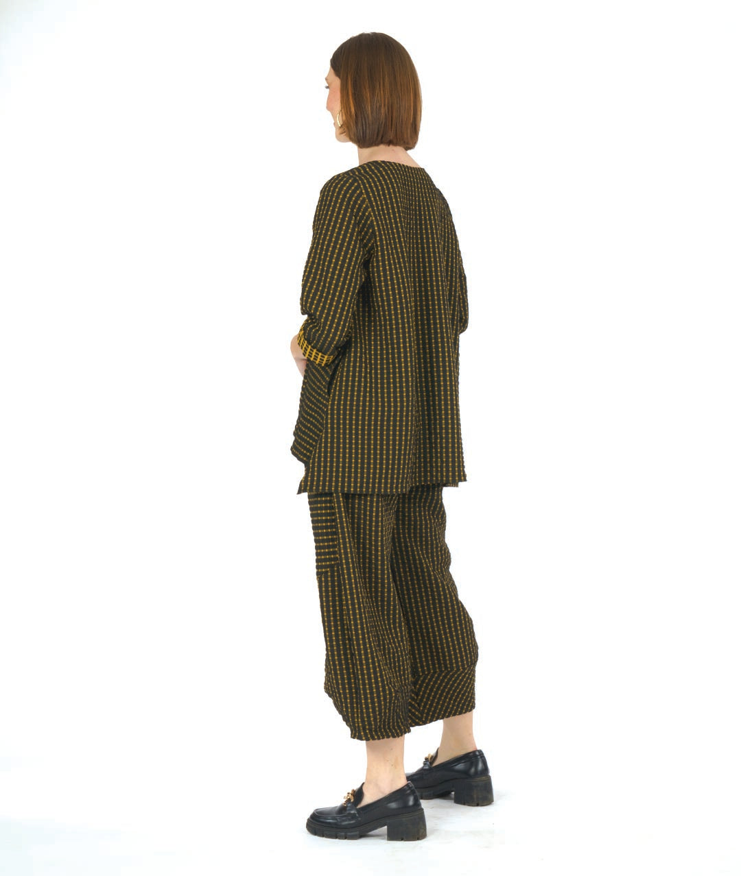 model in a black and yellow check print pullover top with contrasting panels and a v-neck. worn with a matching wide leg pant with an oversized pocket and tapered ankle