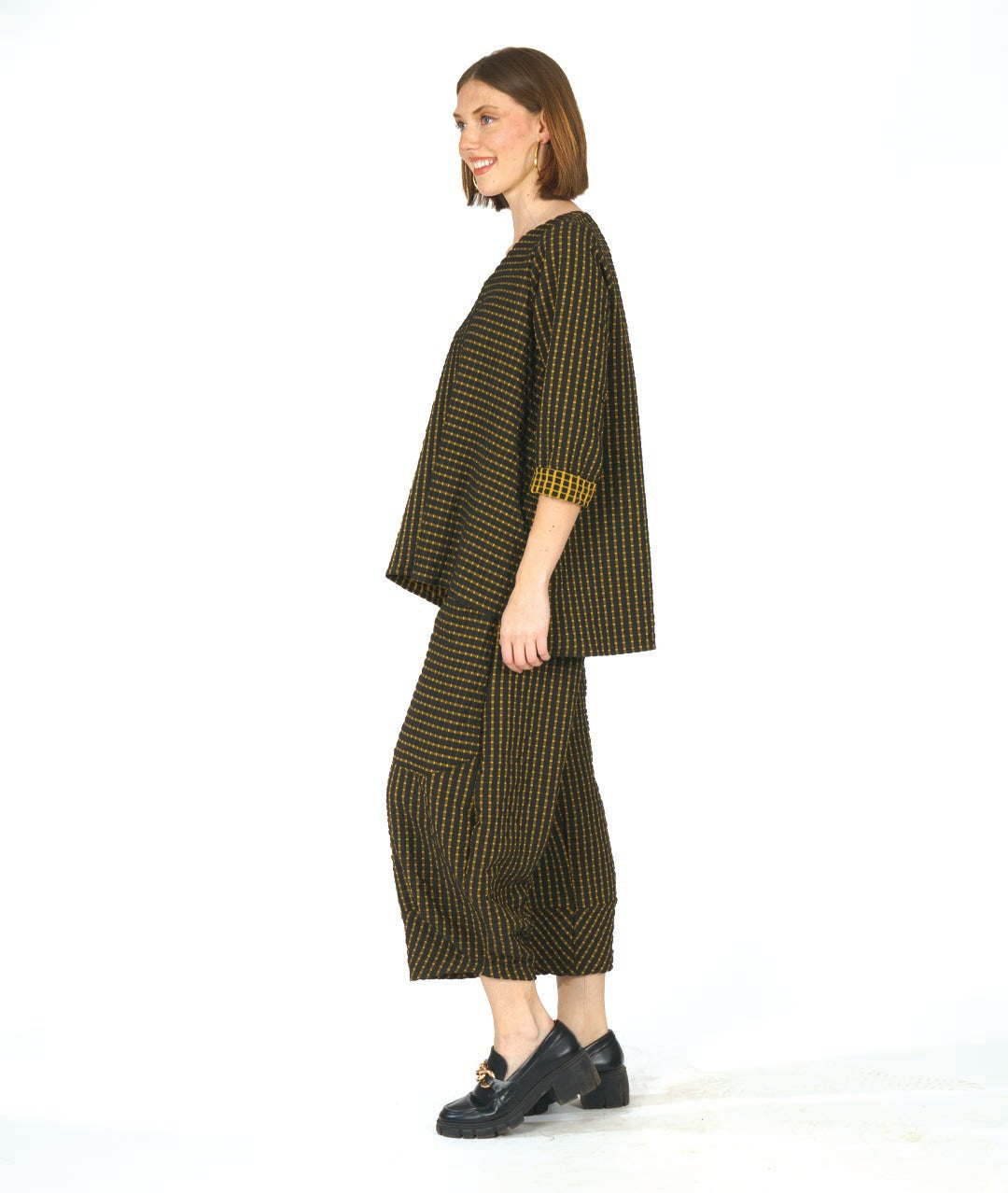 model in a black and yellow check print pullover top with contrasting panels and a v-neck. worn with a matching wide leg pant with an oversized pocket and tapered ankle