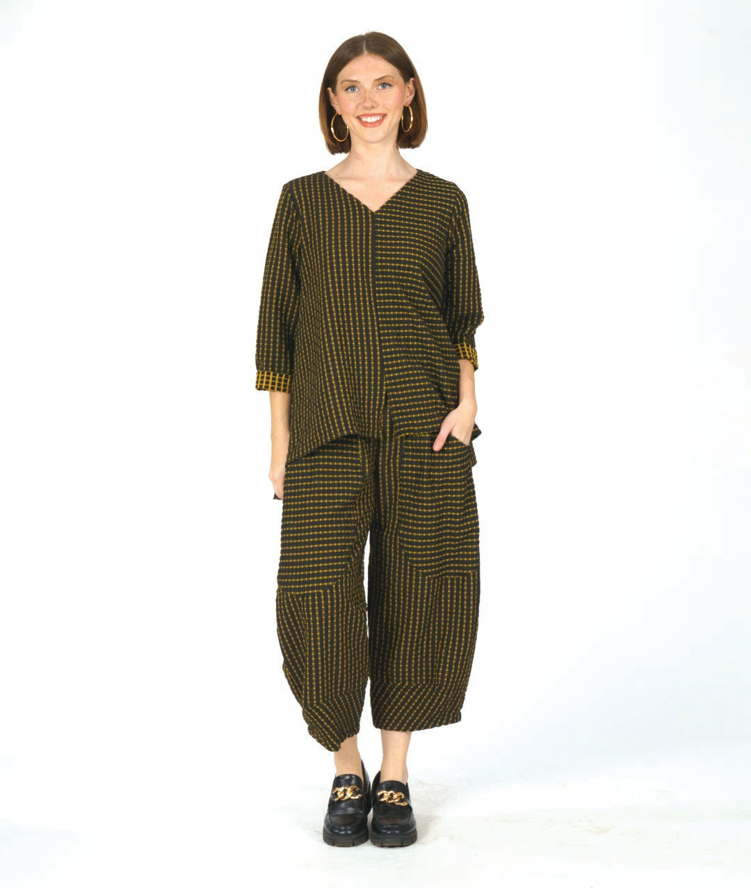 model in a black and yellow check print pullover top with contrasting panels and a v-neck. worn with a matching wide leg pant with an oversized pocket and tapered ankle