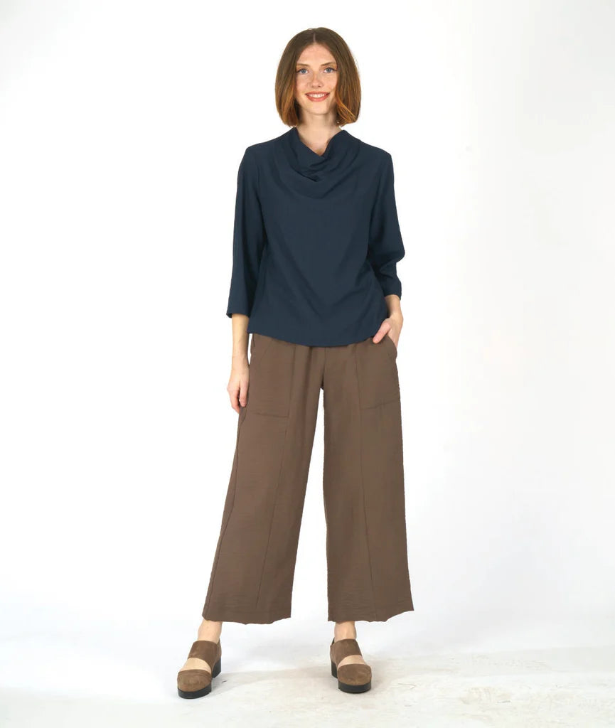 model wearing a navy blue cowl top and brown pants against a white background