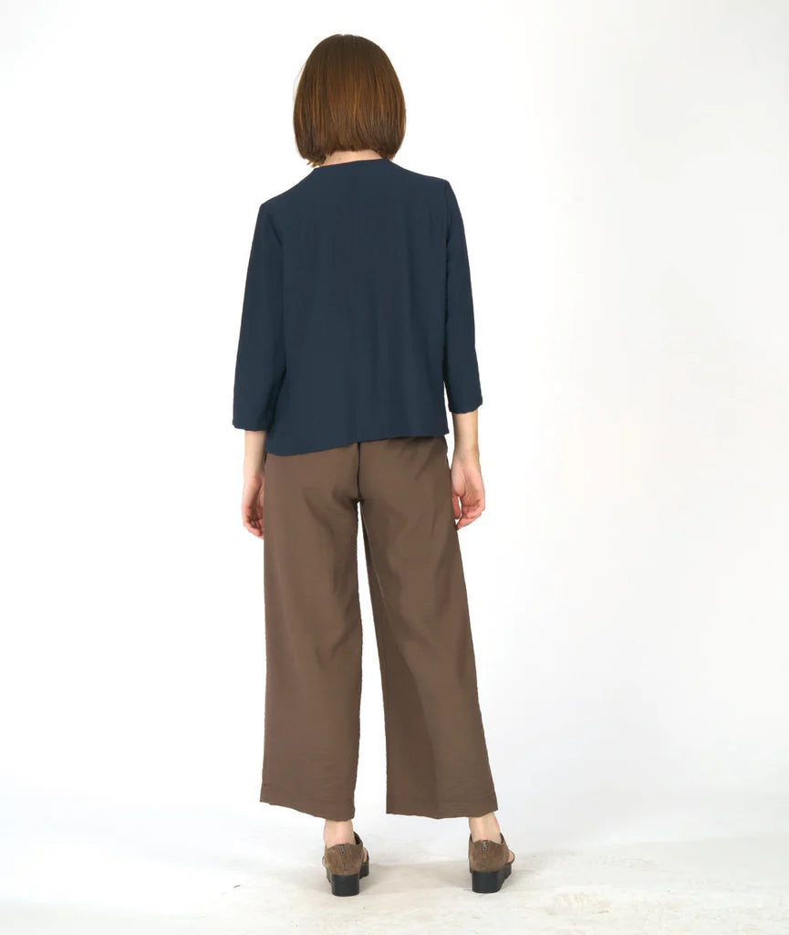 model showing back of navy blue cowl top and brown pants against a white background